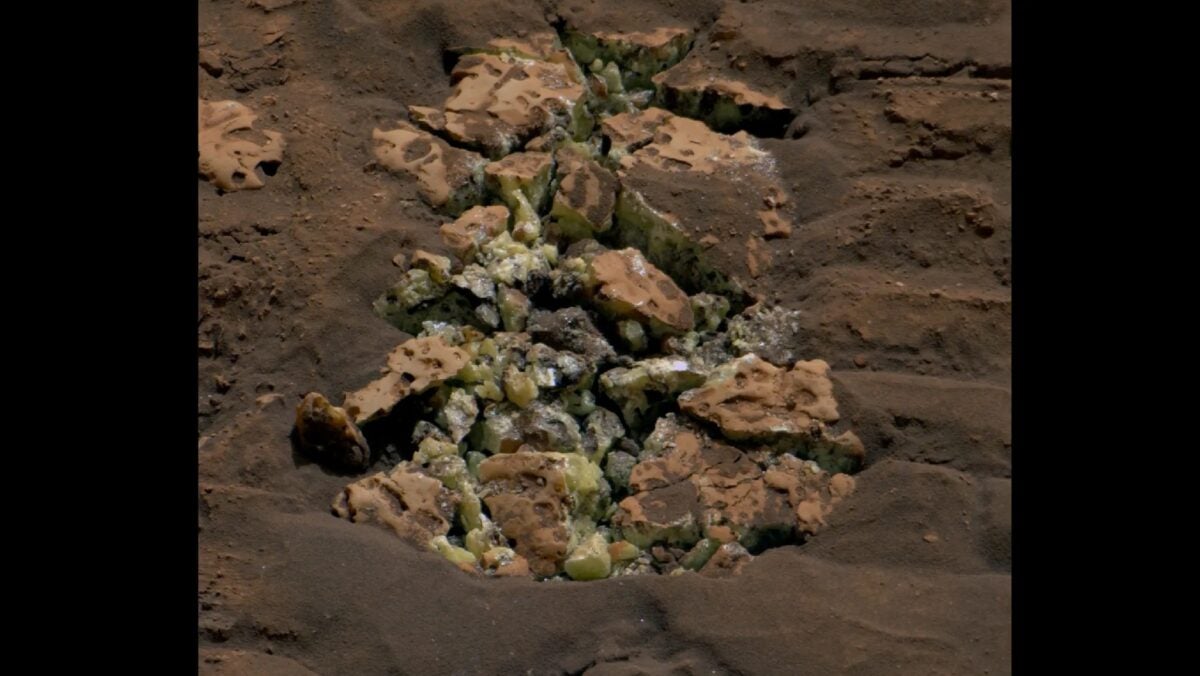 Image of a pile of rocks on Mars. The soil surrounding the rocks is terracotta-colored, and the rocks in the center of the image have yellow crystals on the edges.