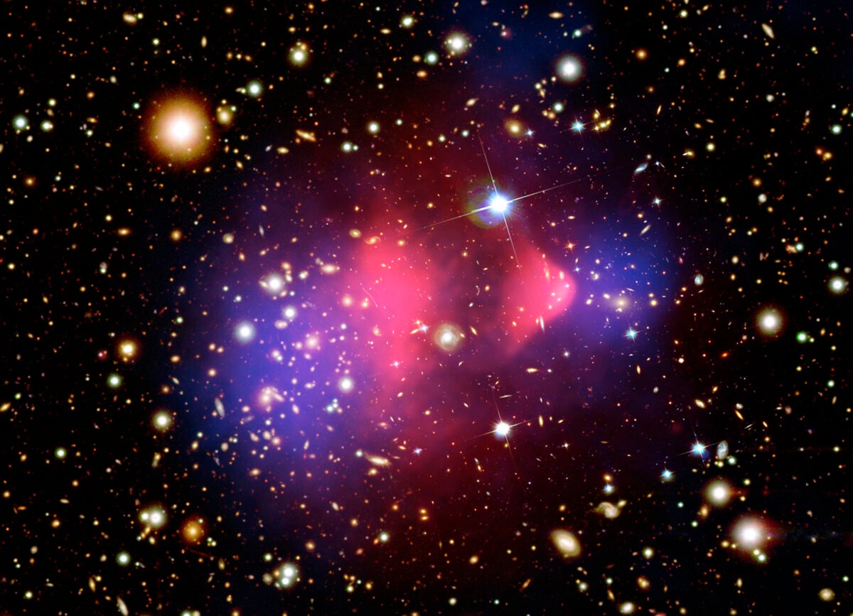 This composite image shows X-rays and visible light from the Bullet Cluster of galaxies, which is made of two separate galaxy clusters colliding. The hot gas associated with the cluster, which comprises most of the normal matter and is visible in X-rays, is colored pink. But the distribution of mass obtained through gravitational lensing is shown in blue — this is the location of the cluster’s dark matter. The disconnect between the two shows that dark matter and normal matter are affected differently by the merger.