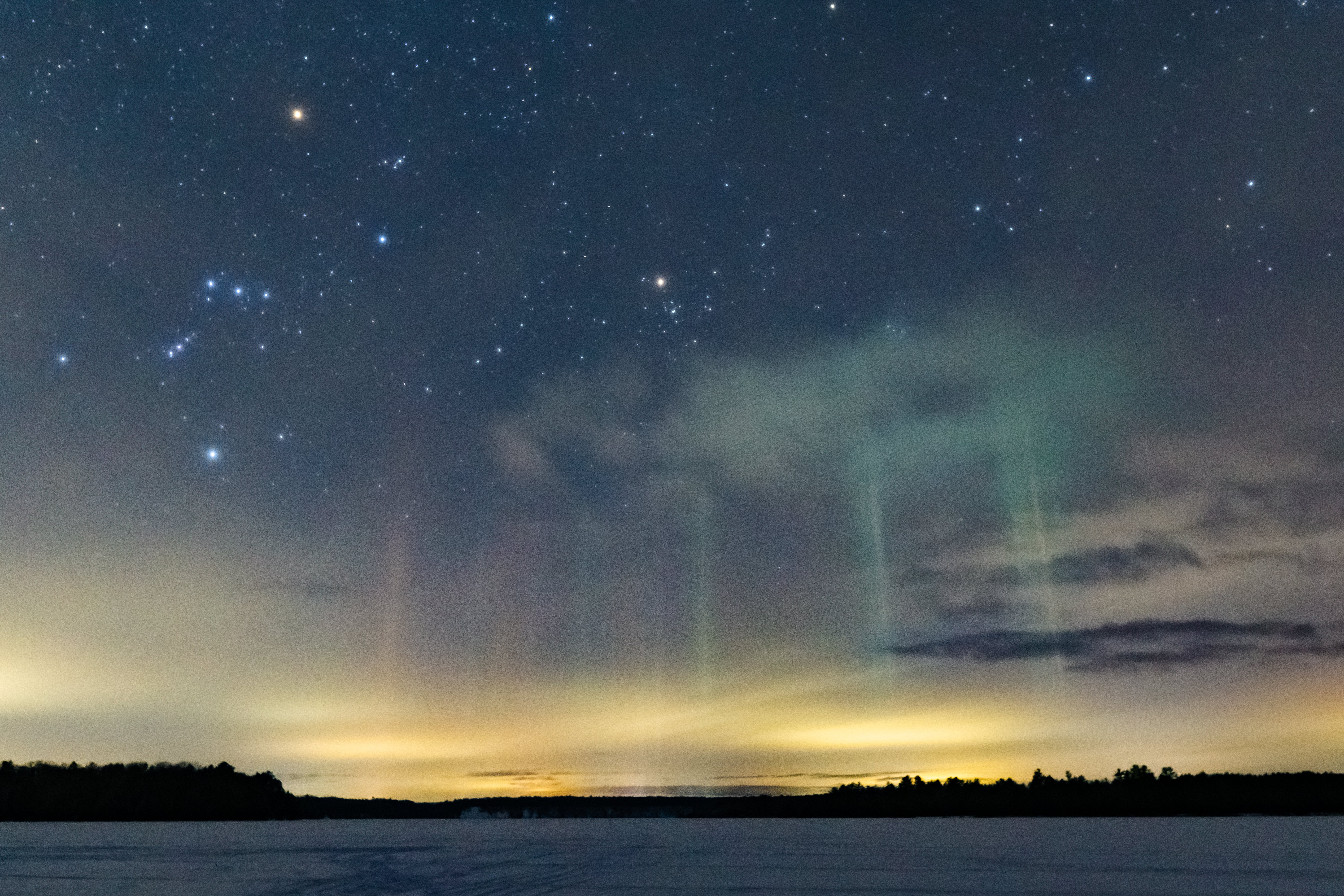 Light pillars appear in the winter sky above a nearby town in this winter scene in northern Michigan. The phenomenon is due to ice crystals in the atmosphere that reflect light. This 20-second exposure was taken with a Sony a6000 mirrorless camera and 16mm prime lens at f/2.5 and ISO 6400.